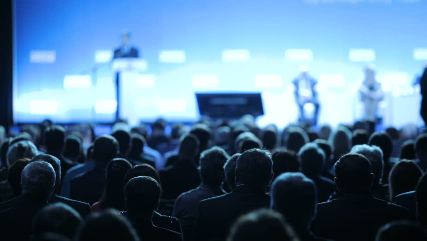 Image depicts a speaker on stage in front of a large crowd, meant to depict someone presenting the development of customizable asset integrity management platform, Antea.
